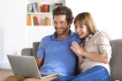 Küchenstudio Ein Mann und eine Frau sitzen auf einer Couch und stöbern in Online-Katalogen nach Küchengeräten.