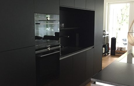 Küchenstudio Referenzen: Eine Küche mit schwarzen Schränken und Holzboden.