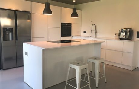 Küchenstudio Eine weiße Küche mit Küchengeräten und Hockern aus Edelstahl, ausgestattet mit modernen Referenzen.