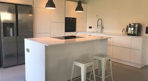 Küchenstudio Eine weiße Küche mit Küchengeräten und Hockern aus Edelstahl, ausgestattet mit modernen Referenzen.