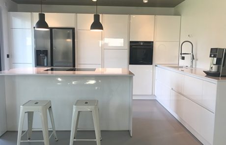 Küchenstudio Eine weiße Küche mit Geräten und Hockern aus Edelstahl, die unsere exquisiten Referenzen präsentiert.