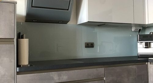Küchenstudio Eine grau-weiße Küche mit Geräten aus Edelstahl, die modernes Design und hochwertige Materialien zur Geltung bringt. Die stilvolle Kombination aus neutralen Farbtönen schafft einen optisch ansprechenden Raum, während die Geräte aus Edelstahl einen Hauch von Eleganz verleihen