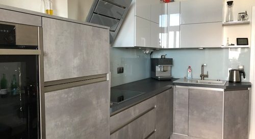 Küchenstudio Eine kleine Küche mit grauen Schränken und Geräten aus Edelstahl. Die Referenzen für diese Küche unterstreichen ihr schlichtes Design und ihre moderne Ausstrahlung.