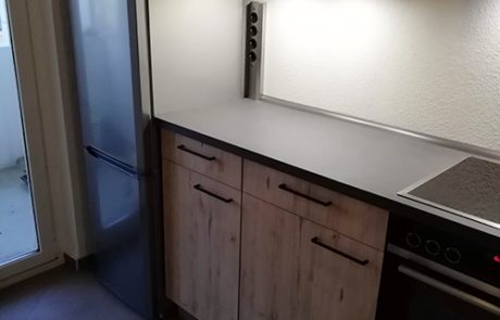 Küchenstudio Eine kleine Küche mit Holzschränken und einem Kühlschrank.