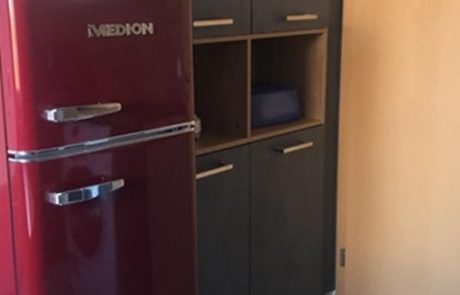 Küchenstudio Ein roter Kühlschrank steht neben einer Tür in einer kleinen Küche.