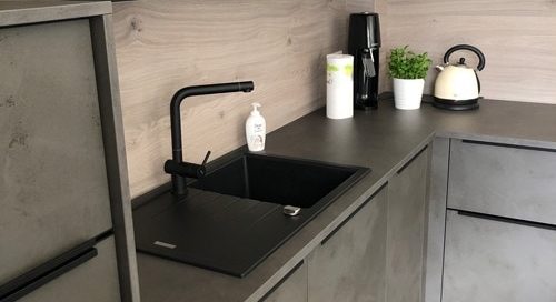 Küchenstudio Referenzen: Eine Küche mit grauen Schränken und einem schwarzen Waschbecken.