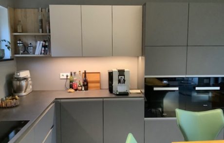 Küchenstudio Referenzen: Eine moderne Küche mit grauen Schränken und grünen Stühlen, die die neuesten Designtrends präsentiert.