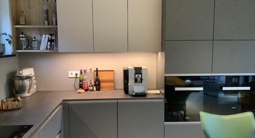 Küchenstudio Referenzen: Eine moderne Küche mit grauen Schränken und grünen Stühlen, die die neuesten Designtrends präsentiert.