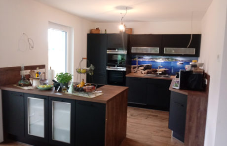 Küchenstudio Referenzen: In diesem Design wird eine Küche mit schwarzen Schränken und einem Holzboden präsentiert.