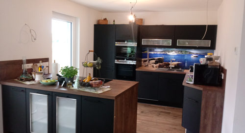 Küchenstudio Referenzen: In diesem Design wird eine Küche mit schwarzen Schränken und einem Holzboden präsentiert.