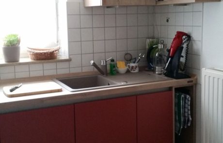 Küchenstudio Eine kleine Küche mit roten Schränken und einer Spüle, inspiriert von modernen Referenzen.