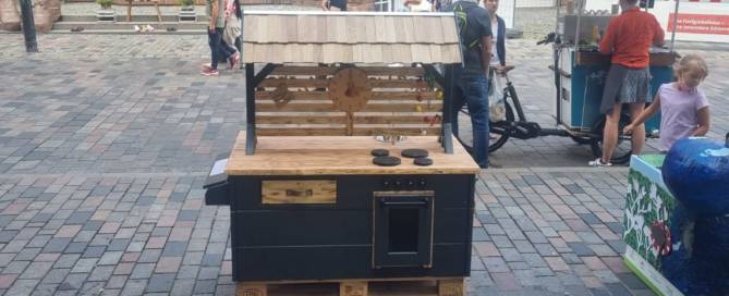 Küchenstudio Eine kleine Küche aus Paletten auf einer Kopfsteinpflasterstraße.