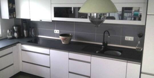 Küchenstudio Eine Küche mit weißen Schränken und schwarzen Arbeitsplatten.