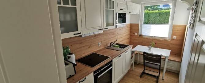 Küchenstudio Eine kleine Küche mit weißen Schränken und Holzböden.