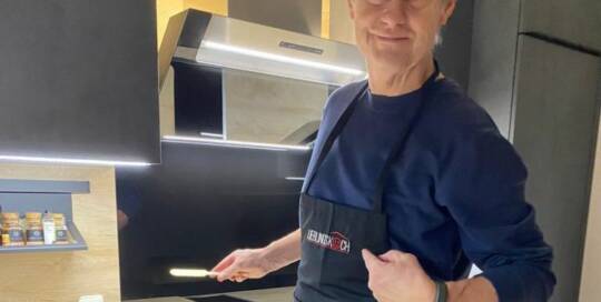 Küchenstudio Ein Mann in einer Schürze steht vor einer Küche.