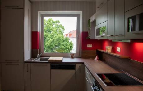 Küchenstudio Eine kleine Küche mit roten Akzenten und einem Fenster.