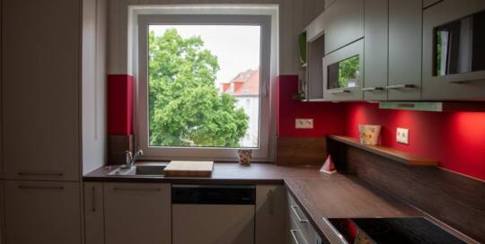 Küchenstudio Eine kleine Küche mit roten Akzenten und einem Fenster.