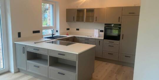 Küchenstudio Eine Küche mit grauen Schränken und Holzboden.