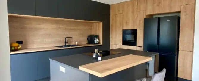 Küchenstudio Moderne Küche mit mattschwarzen Schränken, Holzakzenten, einer Insel mit zwei Hockern, Einbaugeräten und einem schwarzen Kühlschrank.