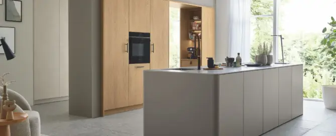 Küchenstudio Dieses moderne Küchenstudio besticht durch eine Kochinsel, einen integrierten Backofen und elegante Schränke. Ein großes Fenster lässt den Fliesenboden in natürliches Licht tauchen. Ein gemütlicher Teppich und ein Stuhl in der Ecke machen es zu einer der Lieblingsküchen für jeden Kochbegeisterten.