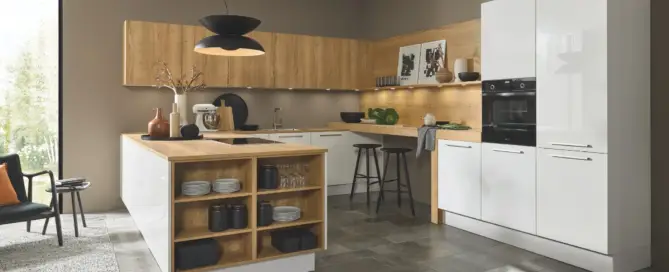 Küchenstudio Dieses moderne Küchenstudio setzt Ihre Lieblingsküchen-Träume mit weißen Schränken, Holzakzenten und einer zentralen Kücheninsel in Szene. Es verfügt über einen eingebauten Backofen, ein Kochfeld, Regale mit Geschirr, Barhocker, eine schwarze Pendelleuchte und ein großes Fenster für natürliches Licht.