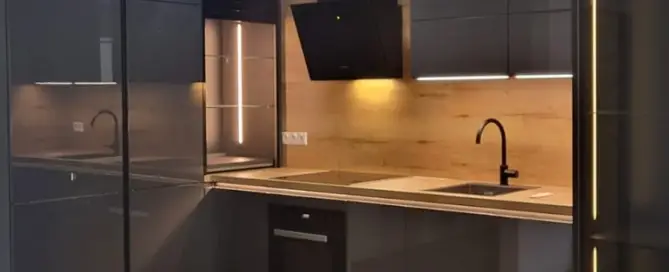 Küchenstudio Moderne Küche mit dunklen Schränken, Holzakzenten und Unterschrankbeleuchtung. Zur Ausstattung gehören ein schwarzer Wasserhahn, ein eingebauter Backofen und ein Herd. Holzboden ergänzt das Design.