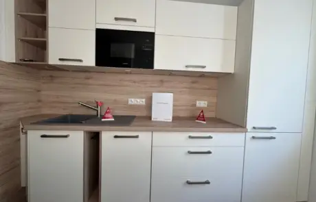Küchenstudio Moderne Küche mit weißen Schränken, Holzarbeitsplatten, einer Spüle, eingebauter Mikrowelle und zwei kleinen roten Warnschildern neben dem Wasserhahn und auf der Arbeitsplatte.
