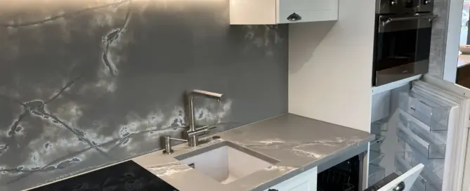 Küchenstudio Moderne Küche mit grauen Marmor-Arbeitsplatten und -Rückwand, weißen Schränken, eingebautem Backofen, Induktionsherd, offenem Geschirrspüler und offenen Kühlschrankschubladen - perfekt für alle, die Qualität in einer Ausstellungsküche abverkaufen möchten.