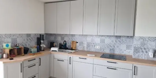 Küchenstudio Moderne Küche mit hellgrauen Schränken, hölzernen Arbeitsplatten, gemusterten Aufkantungen und elektrischem Kochfeld; auf den Arbeitsplatten sind verschiedene Küchenutensilien platziert.