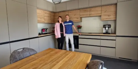 Küchenstudio Zwei Personen stehen zusammen in einer modernen Küche mit hellen und grauen Schränken, neben einem Esstisch aus Holz mit Stühlen.