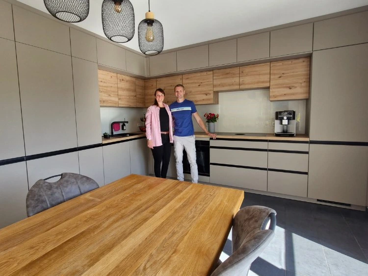 Küchenstudio Zwei Personen stehen zusammen in einer modernen Küche mit hellen und grauen Schränken, neben einem Esstisch aus Holz mit Stühlen.