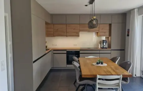 Küchenstudio Moderne Küche mit beigen und hölzernen Schränken, Einbaugeräten, einer Kaffeemaschine und einem Esstisch aus Holz mit sechs Stühlen unter einer schwarzen Pendelleuchte.