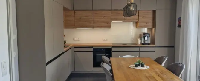 Küchenstudio Moderne Küche mit beigen und hölzernen Schränken, Einbaugeräten, einer Kaffeemaschine und einem Esstisch aus Holz mit sechs Stühlen unter einer schwarzen Pendelleuchte.