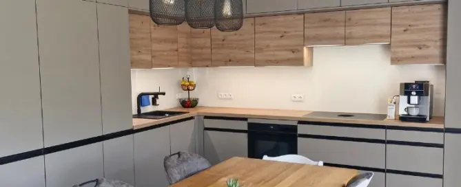 Küchenstudio Moderne Küche mit beigen und hölzernen Schränken, Einbaugeräten, einem Esstisch aus Holz mit Stühlen, Pendelleuchten und einer kleinen Pflanze als Mittelpunkt.