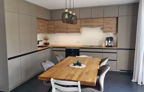 Küchenstudio Moderne Küche mit beigen Schränken, Einbaugeräten, hölzernen Akzenten, einem hölzernen Esstisch mit vier Stühlen, Hängelampen und einem kleinen Pflanzenaufsatz.