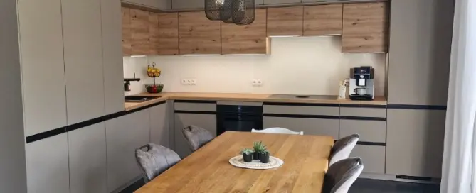 Küchenstudio Moderne Küche mit beigen Schränken, Einbaugeräten, hölzernen Akzenten, einem hölzernen Esstisch mit vier Stühlen, Hängelampen und einem kleinen Pflanzenaufsatz.
