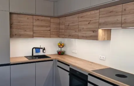 Küchenstudio Moderne Küche mit hellen und grauen Schränken, schwarzer Spüle, eingebautem Backofen, Elektrokochfeld, Obstschale und minimalem Dekor auf einer sauberen Arbeitsplatte.