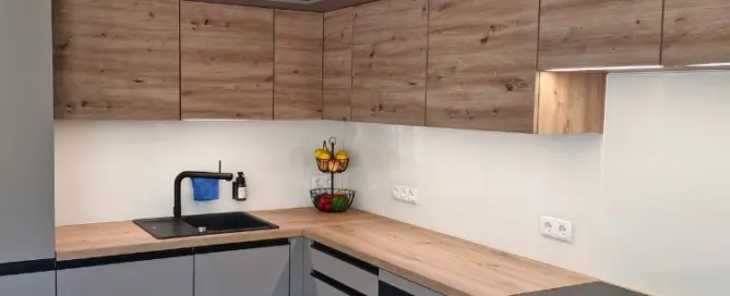 Küchenstudio Moderne Küche mit hellen und grauen Schränken, schwarzer Spüle, eingebautem Backofen, Elektrokochfeld, Obstschale und minimalem Dekor auf einer sauberen Arbeitsplatte.