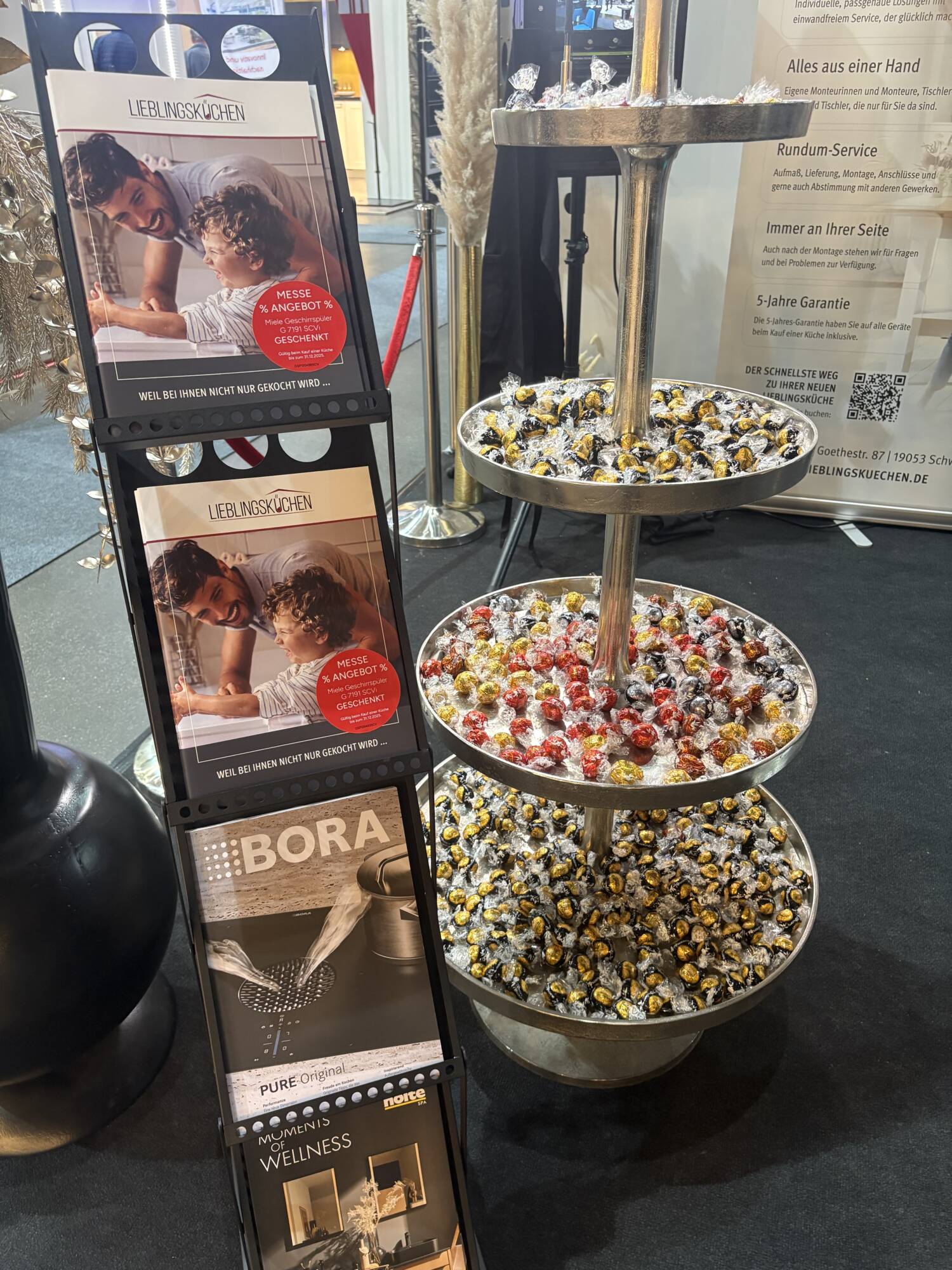 Küchenstudio Aufsteller mit Broschüren und Magazinen neben einem dreistöckigen Tablett mit verpackten Bonbons für eine Veranstaltung oder Ausstellung in Gebäuden.