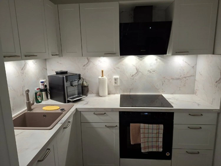 Küchenstudio Moderne Küche mit weißen Schränken und Marmorsockel, mit Spüle, Kaffeemaschine, Papierhandtuchhalter, Elektroherd, Backofen und Unterschrankbeleuchtung.