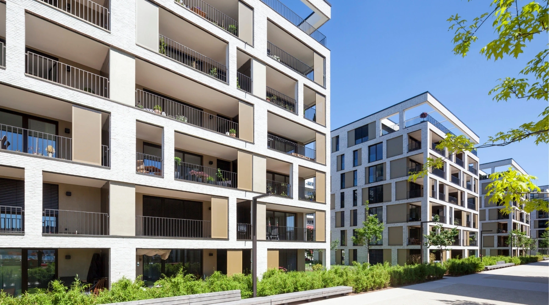 Küchenstudio Moderne Mehrfamilienhäuser mit Balkonen und großen Fenstern, umgeben von viel Grün unter einem strahlend blauen Himmel.