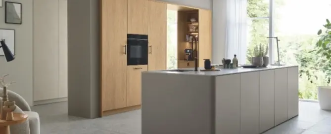 Küchenstudio Moderne Küche mit hellen Holzschränken, Einbaubackofen, offenen Regalen und einer großen grauen Insel mit Spülbecken in einem hellen Raum mit großem Fenster und minimalem Dekor.