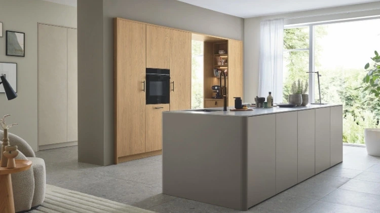 Küchenstudio Moderne Küche mit hellen Holzschränken, Einbaubackofen, offenen Regalen und einer großen grauen Insel mit Spülbecken in einem hellen Raum mit großem Fenster und minimalem Dekor.