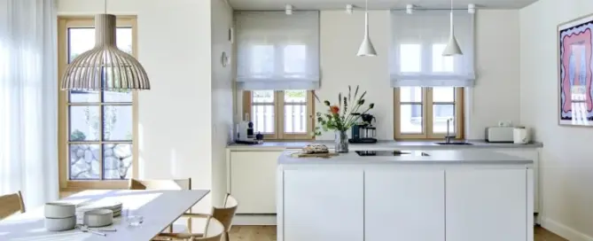 Küchenstudio Moderne Küche mit zentraler Insel, hellem Holzfußboden, Esstisch mit Stühlen, großen Fenstern und minimalistischem weißen Dekor.