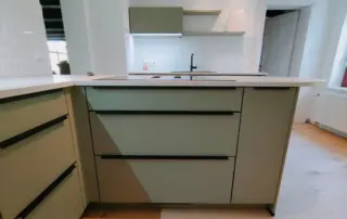 Küchenstudio Moderne Küche mit grünen Schränken, weißen Arbeitsplatten, eingebautem Herd, weißem Subway-Kachelsockel und hellem Holzfußboden. Küchenstudio Moderne Küche mit grünen Schränken, weißen Arbeitsplatten, eingebautem Herd, weißem Subway-Kachelsockel und hellem Holzfußboden.