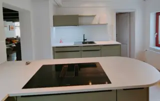 Küchenstudio Moderne Küche mit einer Insel mit Induktionskochfeld, olivfarbenen Schränken, weißen Arbeitsplatten und weißem Fliesenspiegel. Spüle und Wasserhahn befinden sich auf der hinteren Arbeitsplatte. Küchenstudio Moderne Küche mit einer Insel mit Induktionskochfeld, olivfarbenen Schränken, weißen Arbeitsplatten und weißem Fliesenspiegel. Spüle und Wasserhahn befinden sich auf der hinteren Arbeitsplatte.