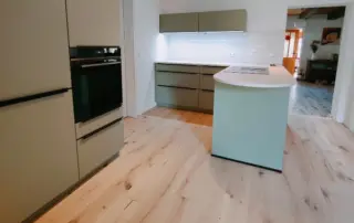 Küchenstudio Moderne Küche mit hellem Holzfußboden, beigen Schränken, Einbaubackofen, Insel mit Kochfeld und weißem Subway-Fliesen-Backsplash unter Schrankbeleuchtung. Küchenstudio Moderne Küche mit hellem Holzfußboden, beigen Schränken, Einbaubackofen, Insel mit Kochfeld und weißem Subway-Fliesen-Backsplash unter Schrankbeleuchtung.