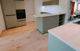 Küchenstudio Moderne Küche mit hellem Holzfußboden, olivgrünen Schränken, einem eingebauten Backofen, einer Insel mit Regalen und weißen Arbeitsflächen. Küchenstudio Moderne Küche mit hellem Holzfußboden, olivgrünen Schränken, einem eingebauten Backofen, einer Insel mit Regalen und weißen Arbeitsflächen.