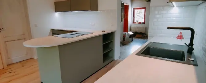 Küchenstudio Moderne Küche mit hellen Arbeitsplatten, Insel mit eingebautem Herd, Unterschrankbeleuchtung, weißer Subway-Fliesenrückwand und Holzfußboden.
