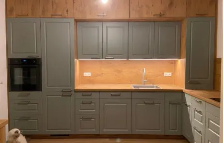 Küchenstudio Moderne Küche mit grauen Schränken, Arbeitsflächen und Aufkantung aus Holz, eingebautem Backofen, Spüle, Unterschrankbeleuchtung und einer Katze, die in der unteren linken Ecke auf dem Boden sitzt.